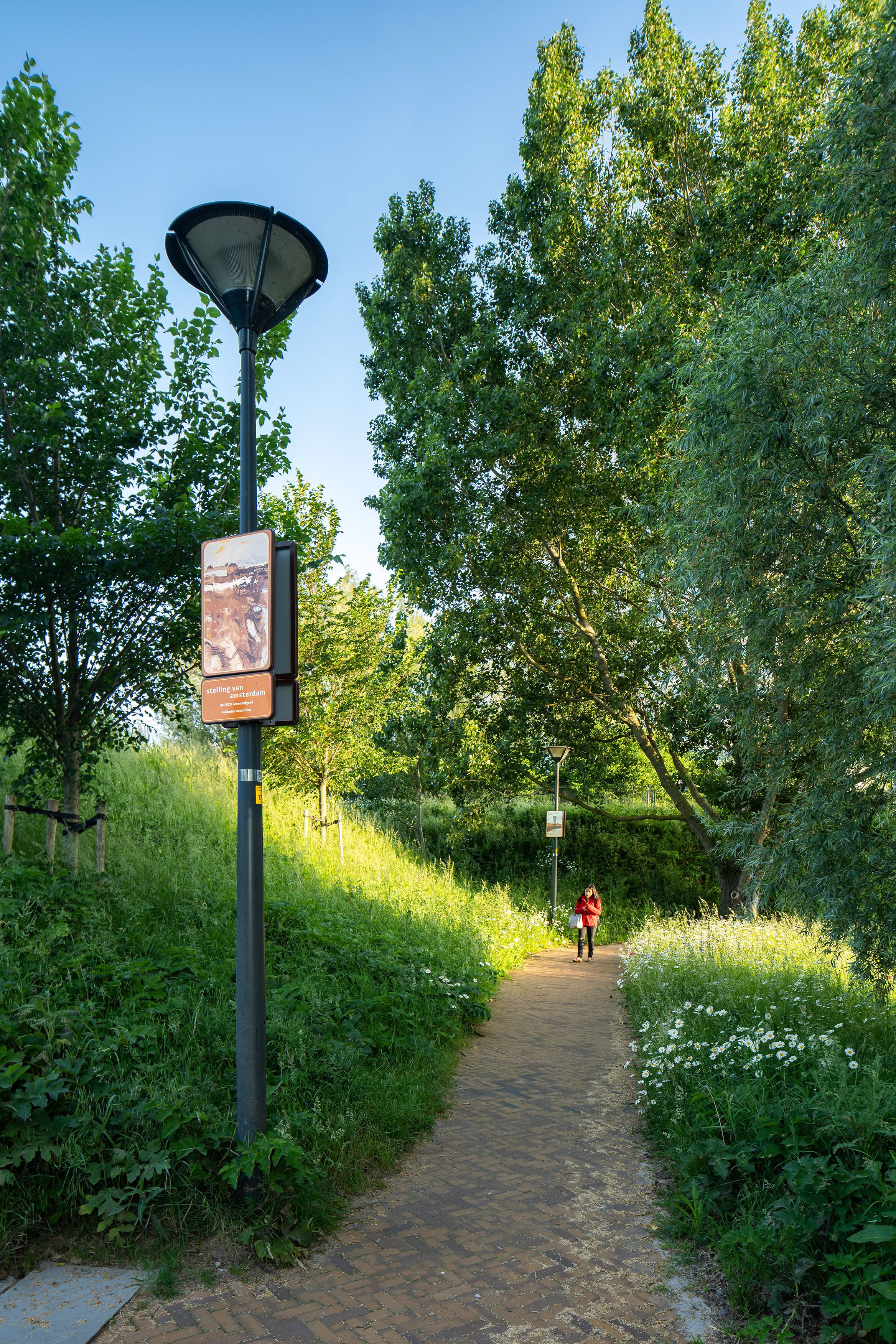 Beeldpaneel Modder en water langs wandelpad op de Geniedijk met wandelaar in rode jas