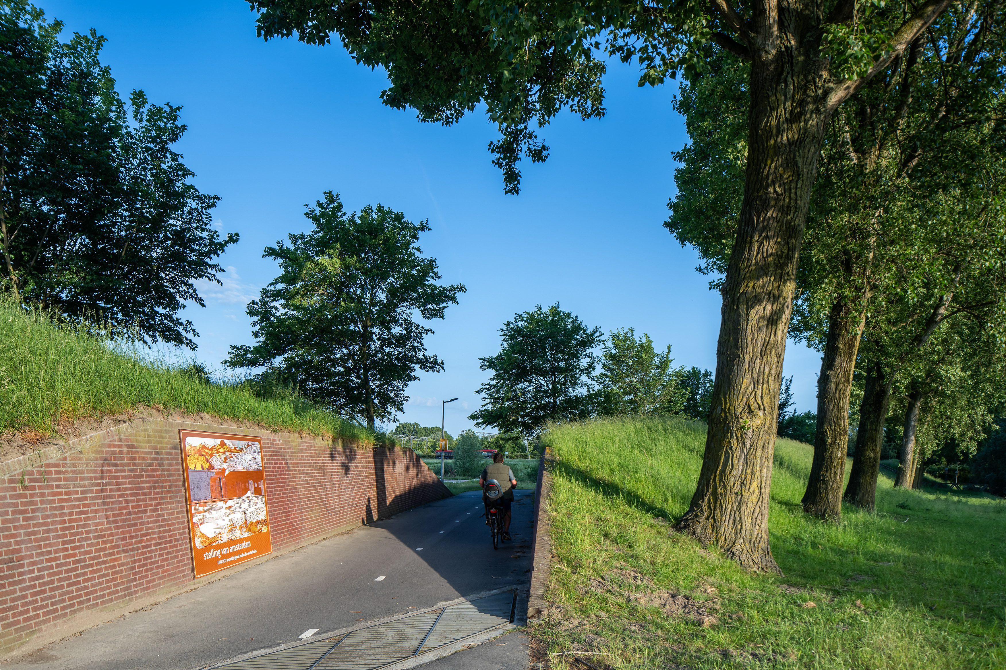 Beeldpaneel De Stelling bij de doorgang door de Geniedijk met passerende fietser