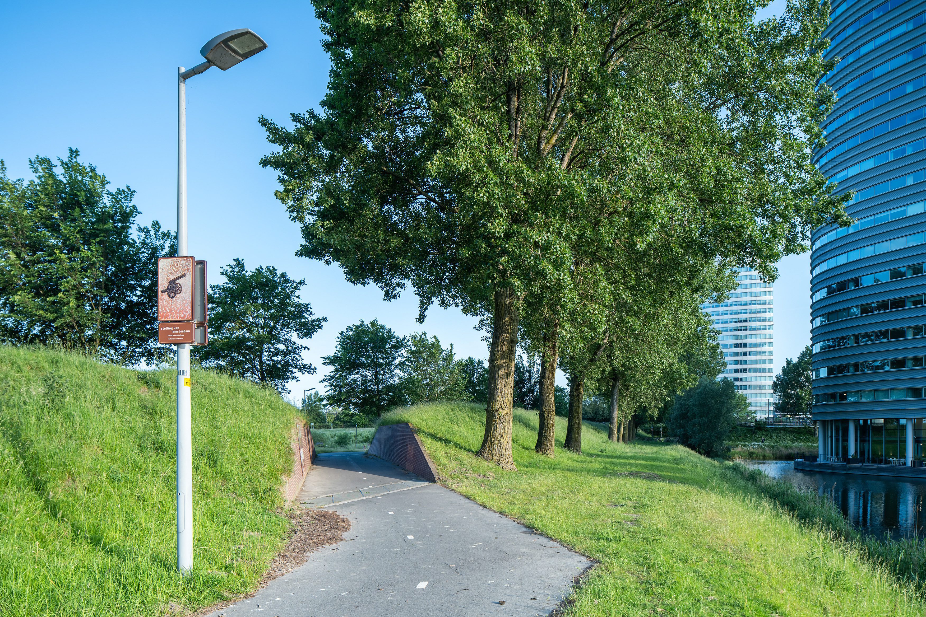 Beeldpaneel Kanon langs de Geniedijk met doorgang door de dijk en moderne kantoorgebouwen op de achtergrond
