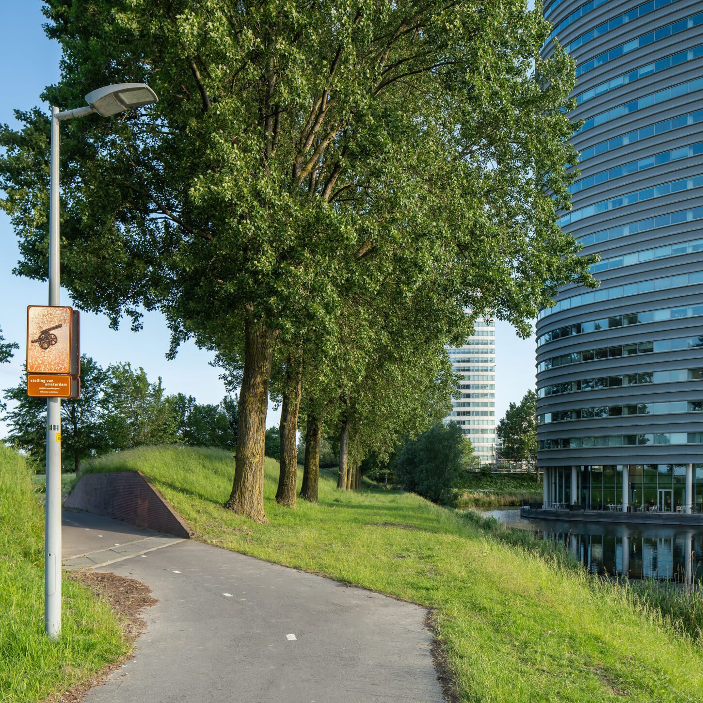 Beeldpaneel Kanon langs de Geniedijk met doorgang door de dijk, watergang en moderne bebouwing van Hoofddorp