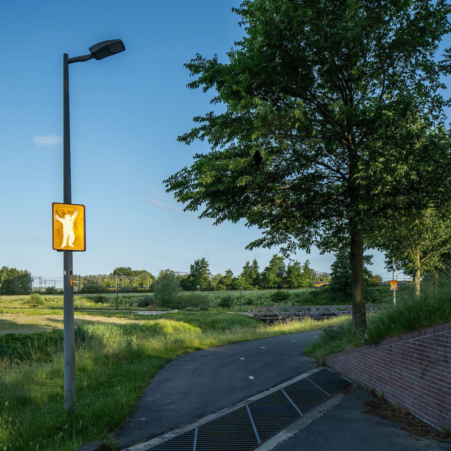 Beeldpaneel De Schreeuw langs de Geniedijk met open landschap, doorgang door de dijk en moderne kantoortoren op de achtergrond