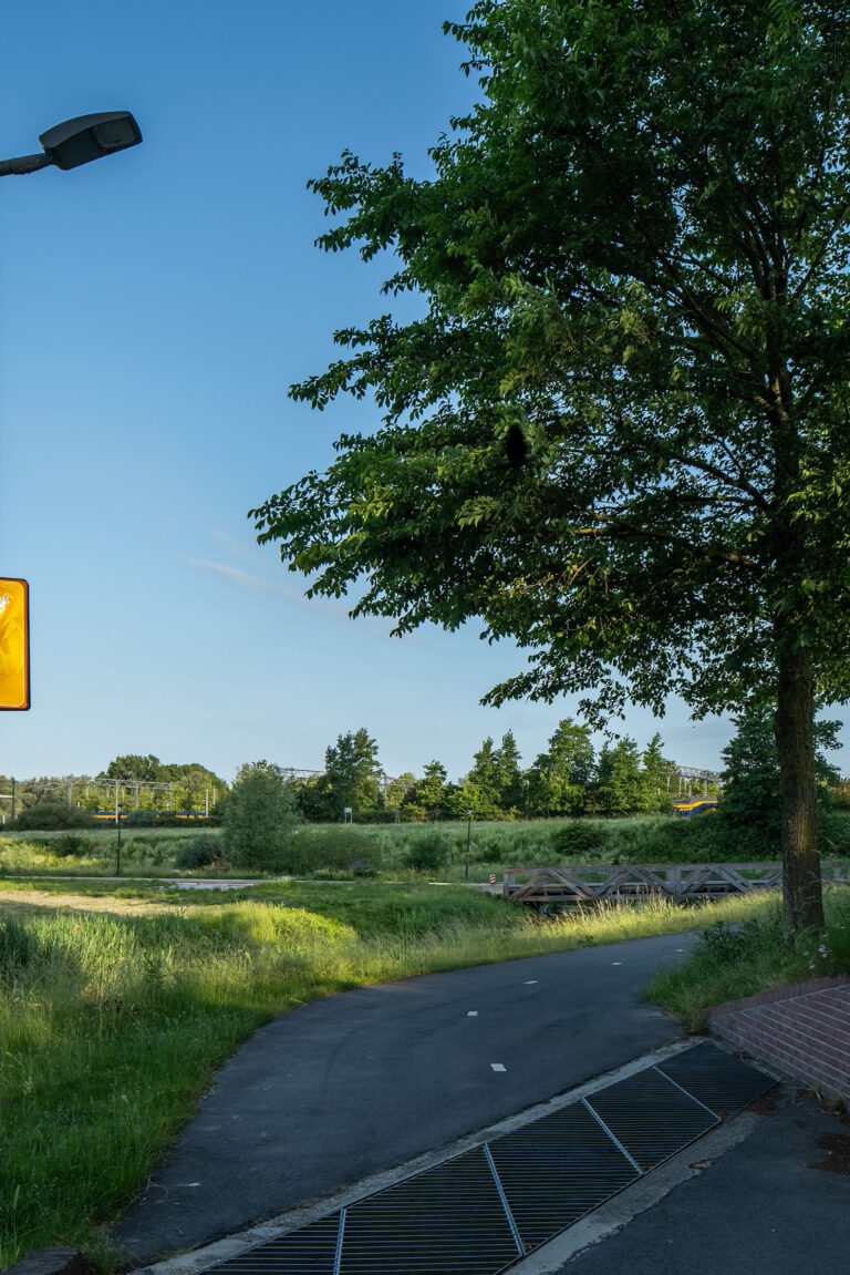Beeldpaneel De Schreeuw langs de Geniedijk met open landschap, doorgang door de dijk en moderne kantoortoren op de achtergrond
