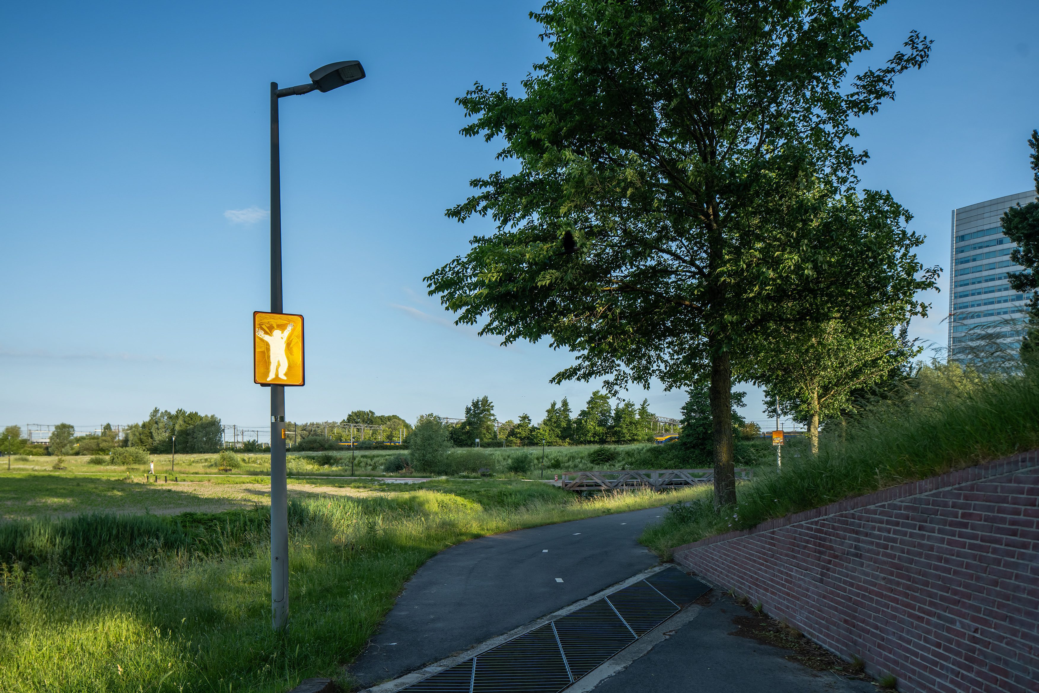 Beeldpaneel De Schreeuw langs de Geniedijk met open landschap, doorgang door de dijk en moderne kantoortoren op de achtergrond