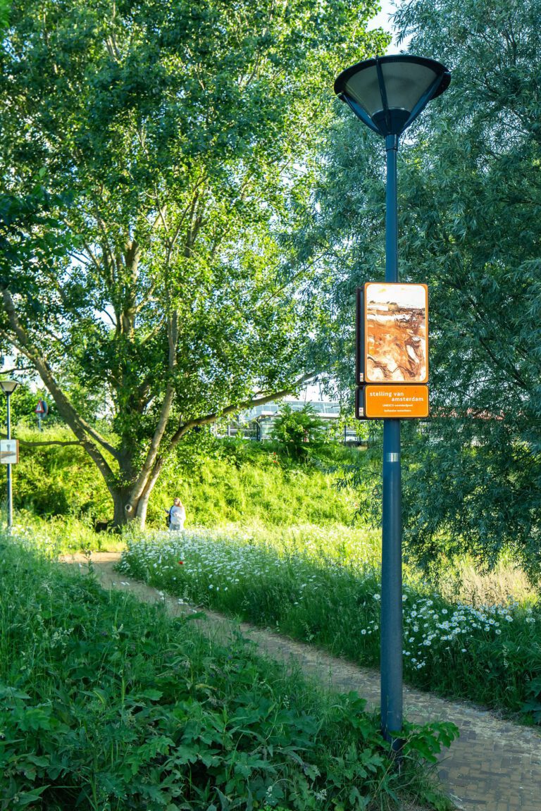 Beeldpaneel Modder en water langs het wandelpad op de Geniedijk tussen bomen en ruige begroeiing