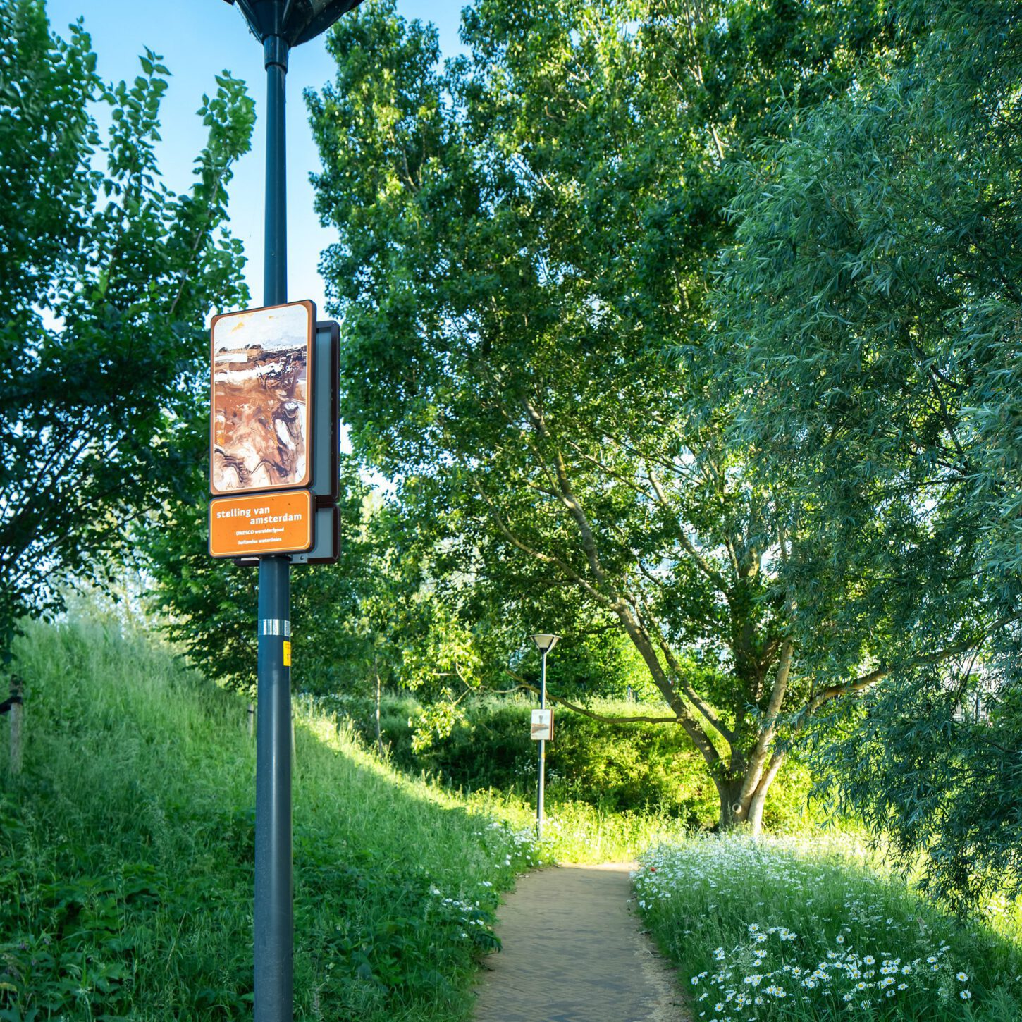 Beeldpaneel Modder en water langs een wandelpad op de Geniedijk met bomen, bloemen en dijkvegetatie